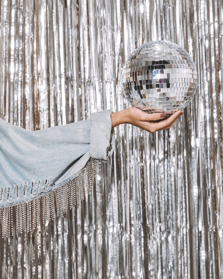 A silver disco ball held in front of a shimmering curtain